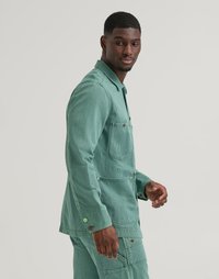 Veste en velours côtelé vert avec un devant à boutons, des poches latérales et un col. Textures notables et rayures verticales. Coupe ajustée.