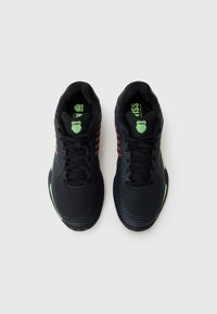 Black athletic shoes with horizontal ribbed texture, green accents, and red detailing. Lace-up design with padded collar and tongue.