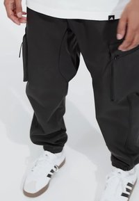 Zwarte cargobroek met ritszakken en een relaxte pasvorm. Aangevuld met witte sneakers met zwarte strepen. Soepele textuur, modern ontwerp.