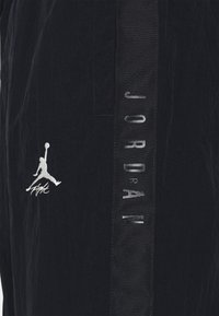 Black athletic shorts with subtle crinkled texture, featuring a silver "Jumpman" logo and "JORDAN" embroidered vertically on the side.