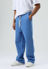 Lichtblauwe sweatpants met een trekkoord, voorzien van zijzakken en een relaxte pasvorm. Gecombineerd met witte sneakers en een losse witte T-shirt.