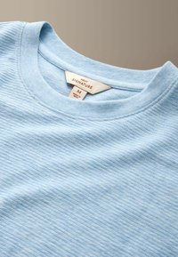 Haut en maille côtelée bleu clair à col rond avec une étiquette Next Signature indiquant la taille M et fabriqué en Inde.