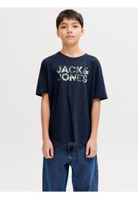 Αγόρι που φοράει μαύρο μπλουζάκι με το λογότυπο "JACK & JONES" και μπλε τζιν, στέκεται μπροστά σε λευκό φόντο.