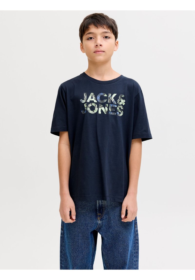 Αγόρι που φοράει μαύρο μπλουζάκι με το λογότυπο "JACK & JONES" και μπλε τζιν, στέκεται μπροστά σε λευκό φόντο.