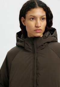 Giacca cappuccio marrone con chiusura a zip, finitura testurizzata e vestibilità rilassata con maniche raglan per una maggiore libertà di movimento.