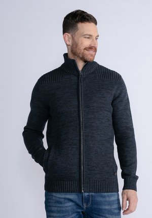 Dunkelgrau gefütterter Reißverschluss-Pullover mit geripptem Kragen und Bündchen, strukturiertem Strickmuster und seitlichen Taschen, getragen über blauen Jeans.