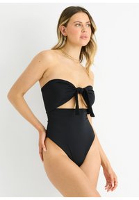 Black one-piece swimsuit featuring a strapless design with a knotted front and high-cut legs. Smooth fabric with a solid color and cut-out detail.