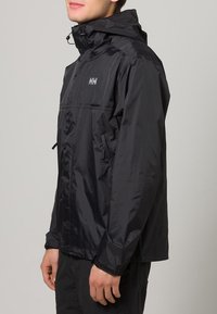 Chaqueta impermeable negra con capucha, cremallera frontal y cordón ajustable. Presenta un logo en el pecho y dos bolsillos laterales.