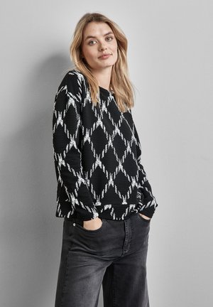 Pull en maille noir avec un motif de diamant blanc et une texture côtelée, associé à un pantalon large gris foncé. Coupe décontractée avec des poches latérales.
