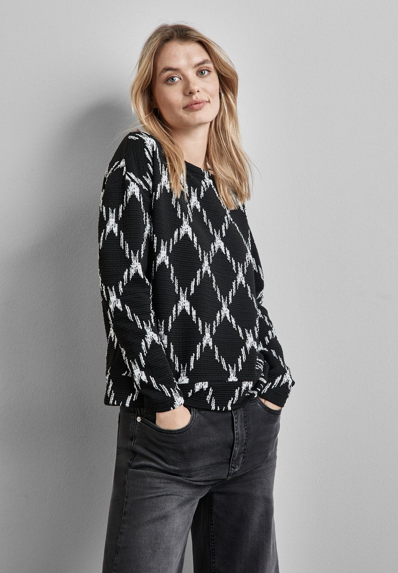 Sort strikket sweater med et hvidt diamantmønster og ribbet tekstur, parret med mørkegrå bukser med vide ben. Casual fit med sidelommer.