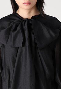 Zwarte blouse met een grote strik-kraag, gemaakt van gladde stof met een lichte glans. Het ontwerp valt loos om de nek.