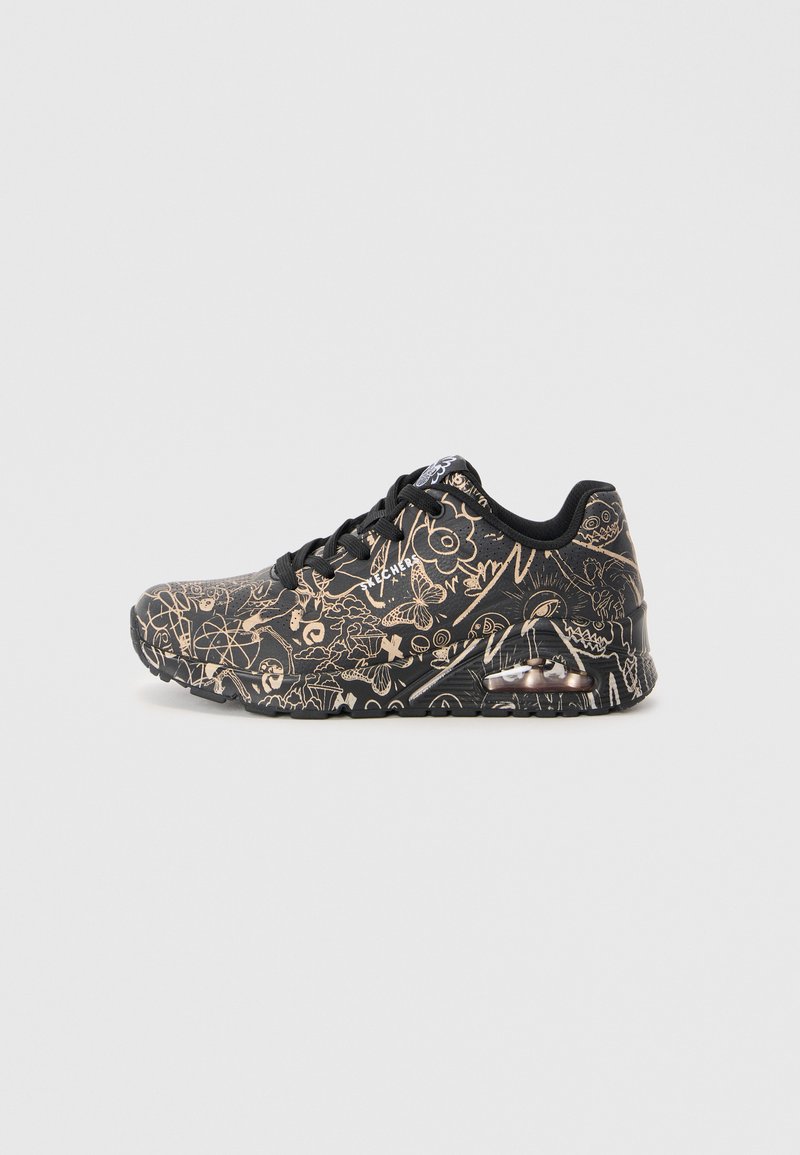 Black sneaker with gold abstract patterns, featuring a cushioned sole, round toe, and lace-up design. Transparent air unit in the heel.