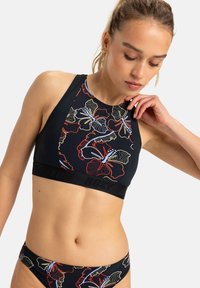 Top de natación negro con estampado floral colorido, escote alto y banda negra ancha con el logo de la marca. Se ven las braguitas de bikini a juego.