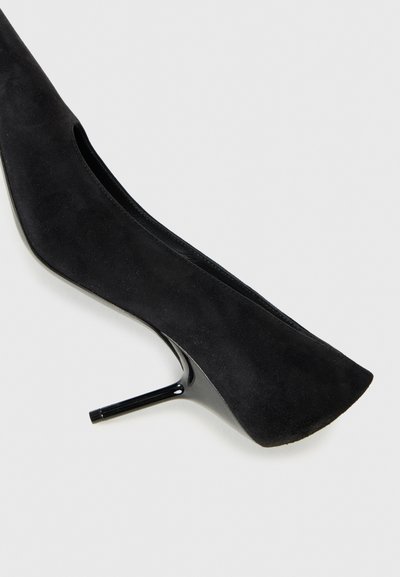 Črne zamšaste stiletto pete s koničastim nosom in gladko, sijočo črno peto. Oblikovanje vključuje nizko rezan vamp za eleganten silhuet.