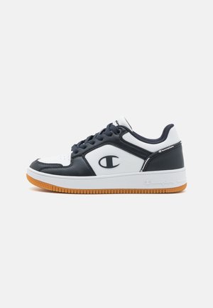 Scarpe atletiche bianche e blu marino con una suola in gomma, caratterizzate da una superficie texturizzata, dettagli cuciti e un logo sul lato.