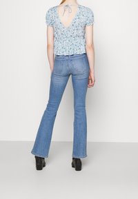 Blå blommig blus med korta puffärmar och V-ringning på ryggen, kombinerad med ljusblå utsvängda jeans. Båda har en figurnära design och denimtextur.