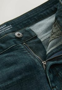 Tumesinised denimpüksid kitseneva lõikega, millel on tõmbluku esitasku, metallist nööbi kinnitust ja mustrilise kangaga vöökoha sisekülg.