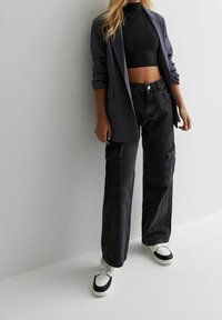 Mustapaita, joka on yhdistetty väljäntuntuisen harmaan bleiserin, farkkukangaspussihousujen ja musta-valkoisten lenkkareiden kanssa. Teksturoitu, rento ja moderni muotoilu.