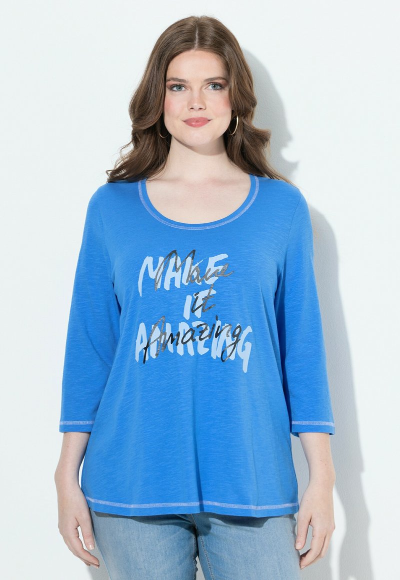 Sininen pitkähihainen paita, jossa on pyöreä kaula-aukko ja viesti "Tee siitä mahtavaa" valkoisella ja mustalla tekstillä; hihassa on kontrastistikkaus.