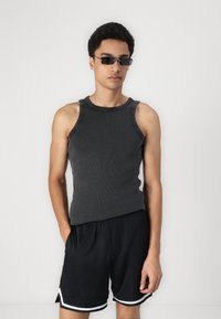 Débardeur gris à côtes associé à un short de sport noir avec des accents blancs. Le mannequin porte des lunettes de soleil noires rectangulaires élégantes.