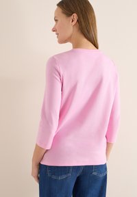 Chemise en coton rose à manches longues avec un col rond et des manches trois-quarts. Texture lisse, design simple, assortie à un jean en denim bleu.