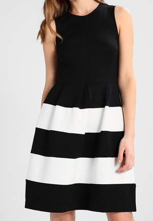 Hihaton musta mekko, jossa vuorottelevat leveät mustat ja valkoiset vaakaraidat hameessa, vyötäröltä istuva, naisen päällä.