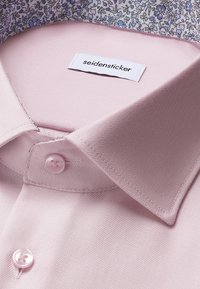 Camicia da uomo rosa chiaro con colletto interno a fiori e etichetta "seidensticker" cucita all'interno del colletto.