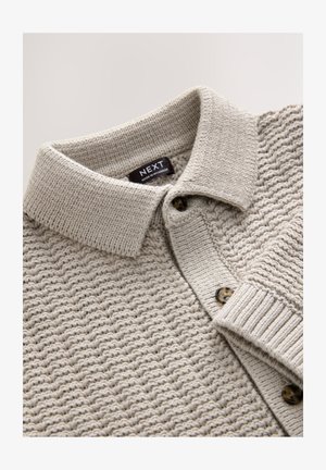 Svetlo siva pletena polo majica z reliefnim vzorcem, z ovratnikom in dvema temnima gumboma. Oznaka pravi "NEXT." Mehki tkan material.
