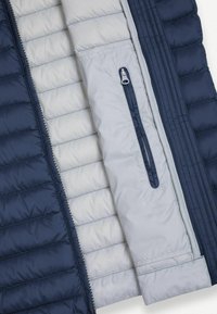 Granatowa i jasno szara pikowana kurtka pokazująca wewnętrzną kieszeń na zamek oraz przeszycia poziomego pikowania.