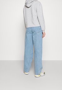 Jeans in denim azzurro chiaro a gamba larga abbinati a un hoodie grigio corto, che mostrano una vestibilità rilassata e tasche posteriori standard.