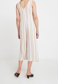 Striped jumpsuit with a v-back, featuring vertical stripes in cream, beige, and blue. Cropped wide legs and lightweight fabric. Black mules.
