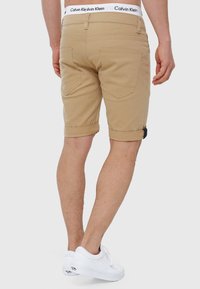 Beige shorts lavet af bomuld, med oprullede manchetter, baglommer og en hvid talje med Calvin Klein-logoet. Bæres med hvide sneakers.