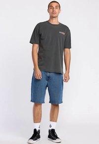 Grey cotton t-shirt with short sleeves, featuring a small red logo, paired with blue denim shorts and black high-top sneakers.