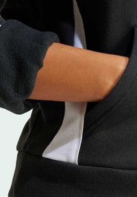 Černá mikina s texturovanou tkaninou, bílým kontrastním panelem a žebrovaným lemem. Rukávová manžeta je mírně zvlněná.