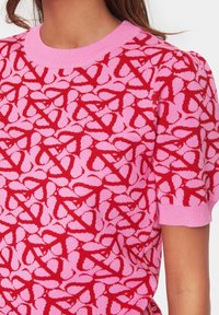 Knit top featuring a red and pink abstract pattern, ribbed crew neckline, and short puff sleeves. Soft texture with a fitted design.