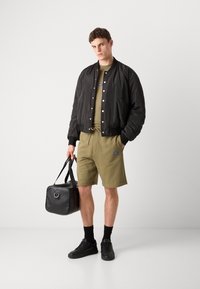 Svart bomberjakke, olivengrønn t-skjorte, matchende shorts, svarte joggesko og en svart treningsbag. Har ribbede mansjetter og snøring i livet.