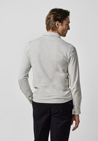 Graues Langarmhemd mit Kragen, mit geknöpften Bündchen und weichem Textil. Die Rückseite zeigt ein schlichtes Design mit minimalen Nähten.