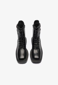 Botas de cuero negro hasta el tobillo con un acabado suave, parte delantera con cordones, suelas acolchadas y una cremallera lateral para facilitar su uso.