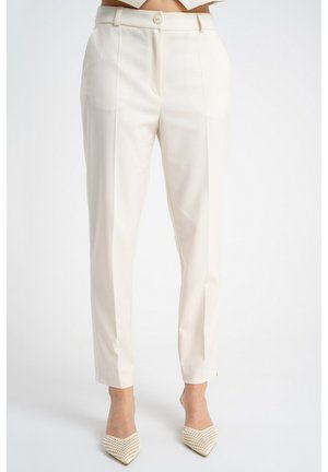 Wąskie, kremowe spodnie o wysokim stanie z przednią fałdą, zapięciem na guzik oraz pasujące, siateczkowe szpilki z noskiem w szpic do kostki.