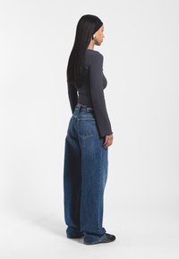 Szerokie niebieskie dżinsy z wysokim stanem, z klasycznym pięcioma kieszeniami. W połączeniu z dopasowaną szaro-skalową bluzką z długim rękawem.