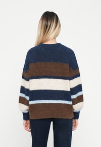 Pull en tricot avec des rayures multicolores en bleu, marron, beige et bleu clair, offrant une coupe ample et des poignets côtelés, en tissu texturé.