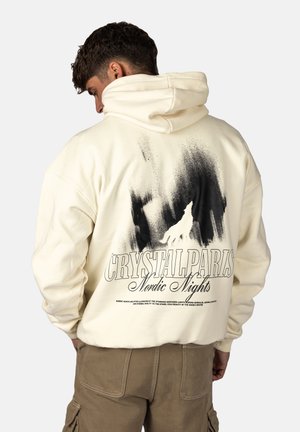 Felpa color crema con stampa grafica nera di un lupo e testo, con vestibilità rilassata e cappuccio grande. Texture morbida e design oversize.