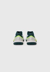 Des chaussures de sport avec une tige vert foncé, des accents argentés et des touches de jaune vif. Semelle en caoutchouc texturé pour une bonne adhérence et durabilité.