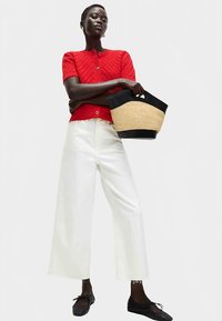 Rode gebreide cardigan, witte broek met wijde pijpen, zwarte platte schoenen, met een ronde strooien tas met een zwart handvat. Patroonstructuur op de trui.