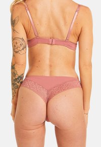 Ensemble de lingerie en dentelle rose comprenant un soutien-gorge avec des bretelles réglables et une culotte assortie mettant en valeur des accents de dentelle florale et une texture géométrique.