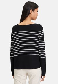 Schwarz-weißer gestreifter Pullover mit weitem Ausschnitt, langen Ärmeln und lockerer Passform. Der Stoff wirkt glatt mit gleichmäßiger Textur.