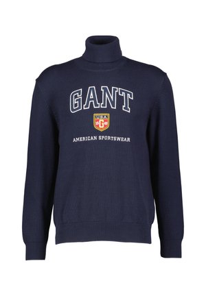 Navy turtleneck sweater made from textured fabric, featuring large white "GANT" logo and shield emblem on the chest.