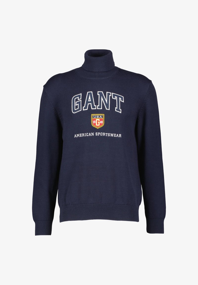 Navy turtleneck sweater made from textured fabric, featuring large white "GANT" logo and shield emblem on the chest.