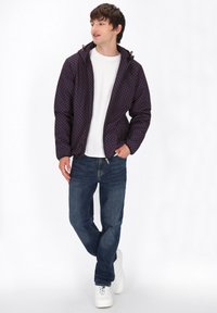 Giacca imbottita con sfondo blu navy e pois rossi a contrasto, dotata di zip frontale e cappuccio. Abbinata a jeans blu e sneakers bianche.