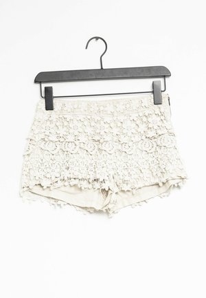 Spitzen-Crochet-Shorts in Off-White mit eingerolltem Saum, floralen Mustern und einer strukturierten Oberfläche mit Pompon-Akzenten, aufgehängt an einem schwarzen Kleiderbügel.
